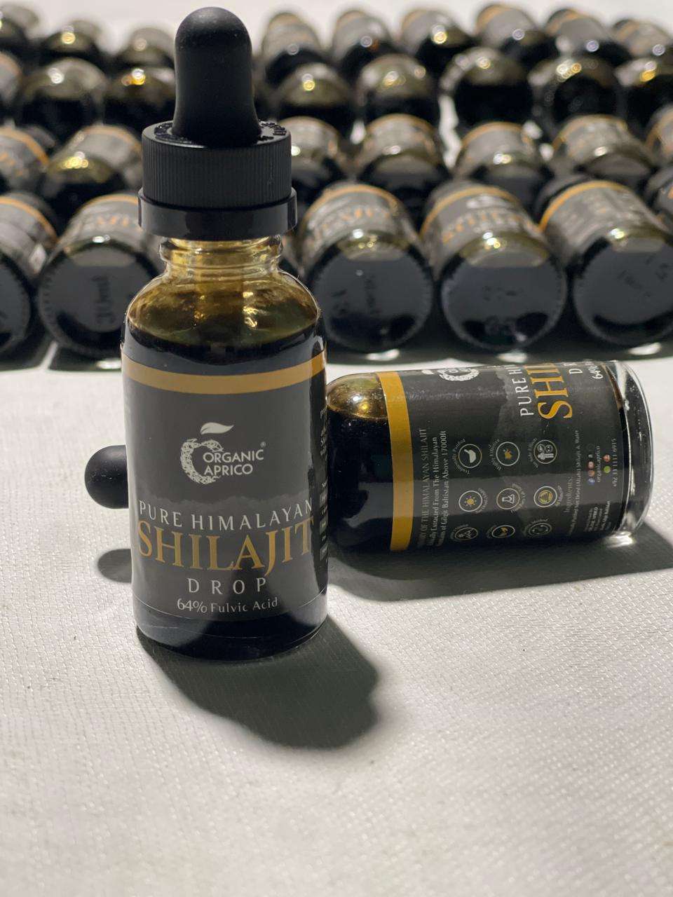 This Picture Shows Shilajit Drop.  Many Shilajit Liquid Bottles in the Background with Organic Aprico LOGO